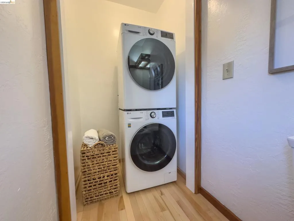 Laundry area featuring stacked appliances and wood-finish flooring