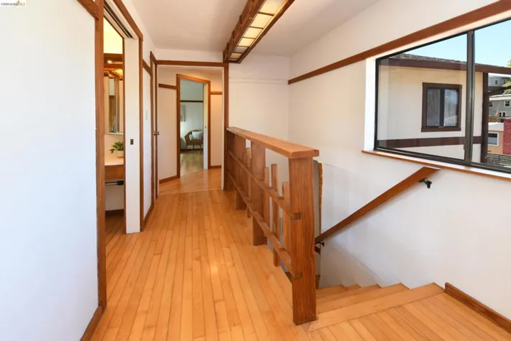 Hardwood flooring throughout this hallway with a window, wood railing, and staircase