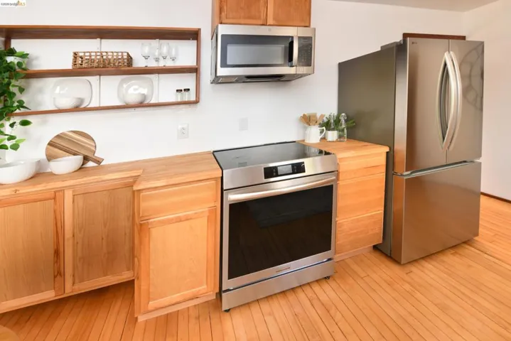 Kitchen featuring stainless steel appliances, wood-finish flooring, light wood cabinetry, butcher block countertops, and open shelving
