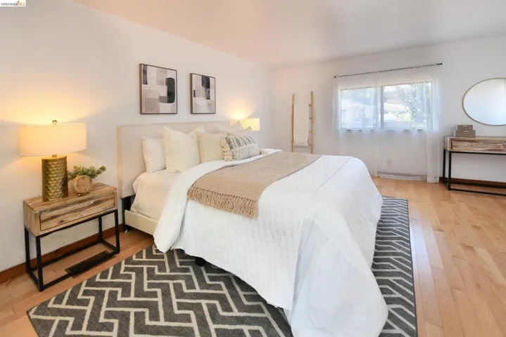 Bright room featuring wood-finish flooring, a large window with sheer curtains, and a light-colored accent wall