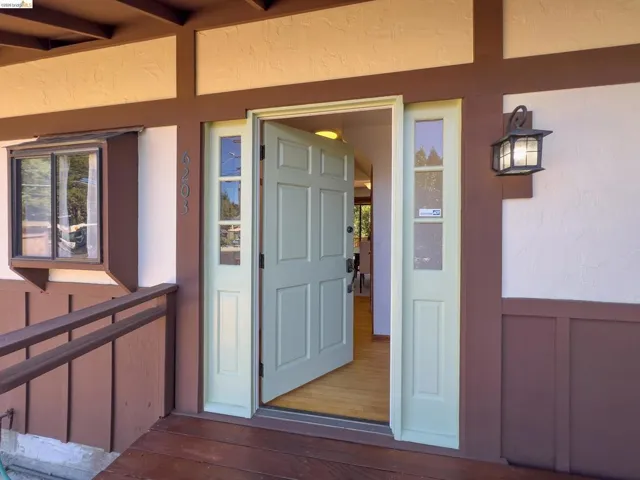 Front entry featuring a light green paneled door, sidelight windows, and a wood-finish porch floor