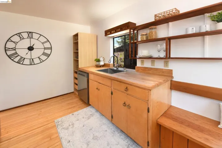 Kitchenette featuring wood-finish flooring, light wood cabinetry, a stainless steel sink with a gooseneck faucet, a built-in dishwasher, and open wood shelving