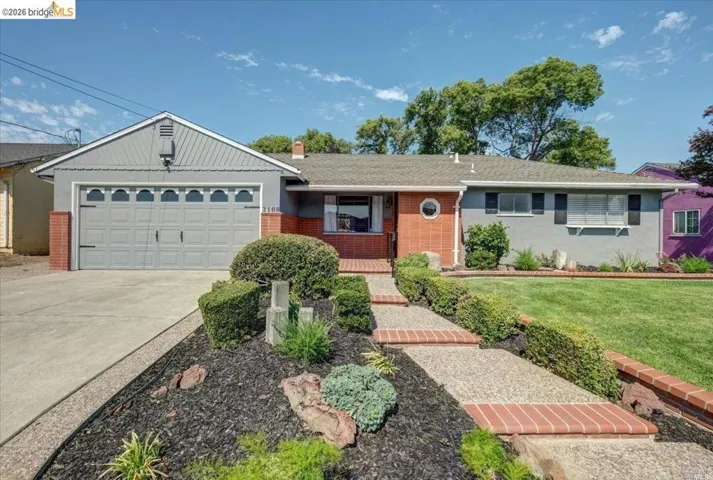 Single-story residence featuring a two-car garage with decorative hardware, a concrete driveway, and a front pathway with brick risers