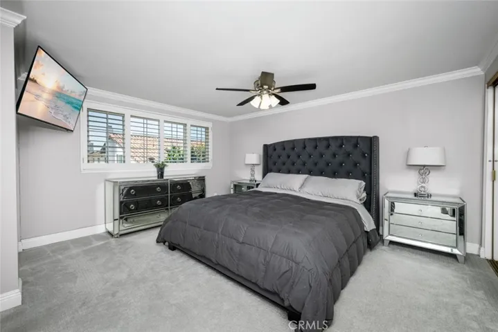 Primary bedroom continues crown molding and timeless plantation shutters.