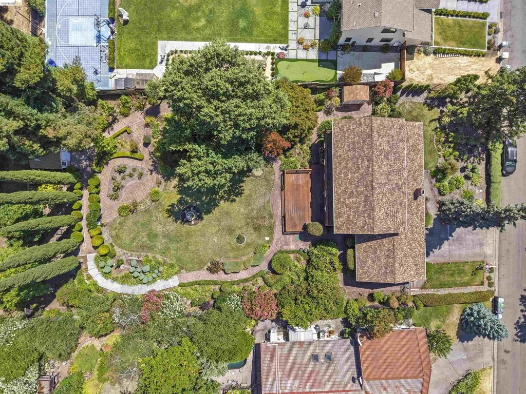 Expansive property with a shingle roof, large mature trees, a manicured lawn, a wooden deck, and extensive landscaping with varied foliage