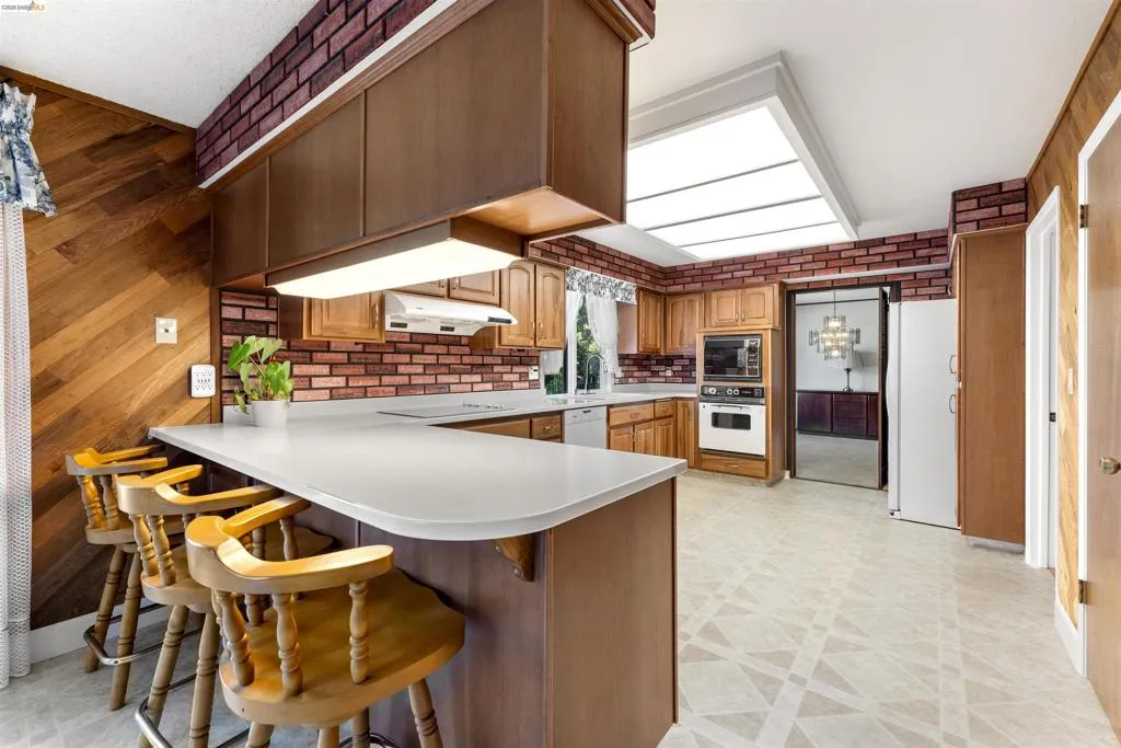 Kitchen featuring a breakfast bar with solid surface countertop, wood-finish cabinetry, a brick-style backsplash, integrated wall oven and microwave, and patterned flooring