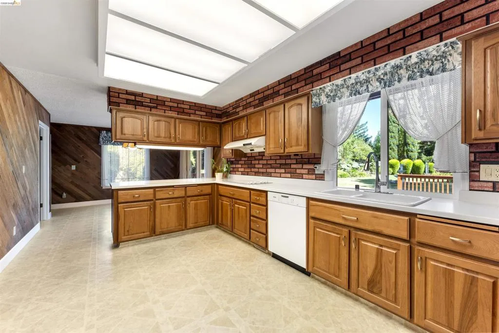 Kitchen featuring wood-finish cabinetry, solid surface countertops, and brick-patterned wall accents