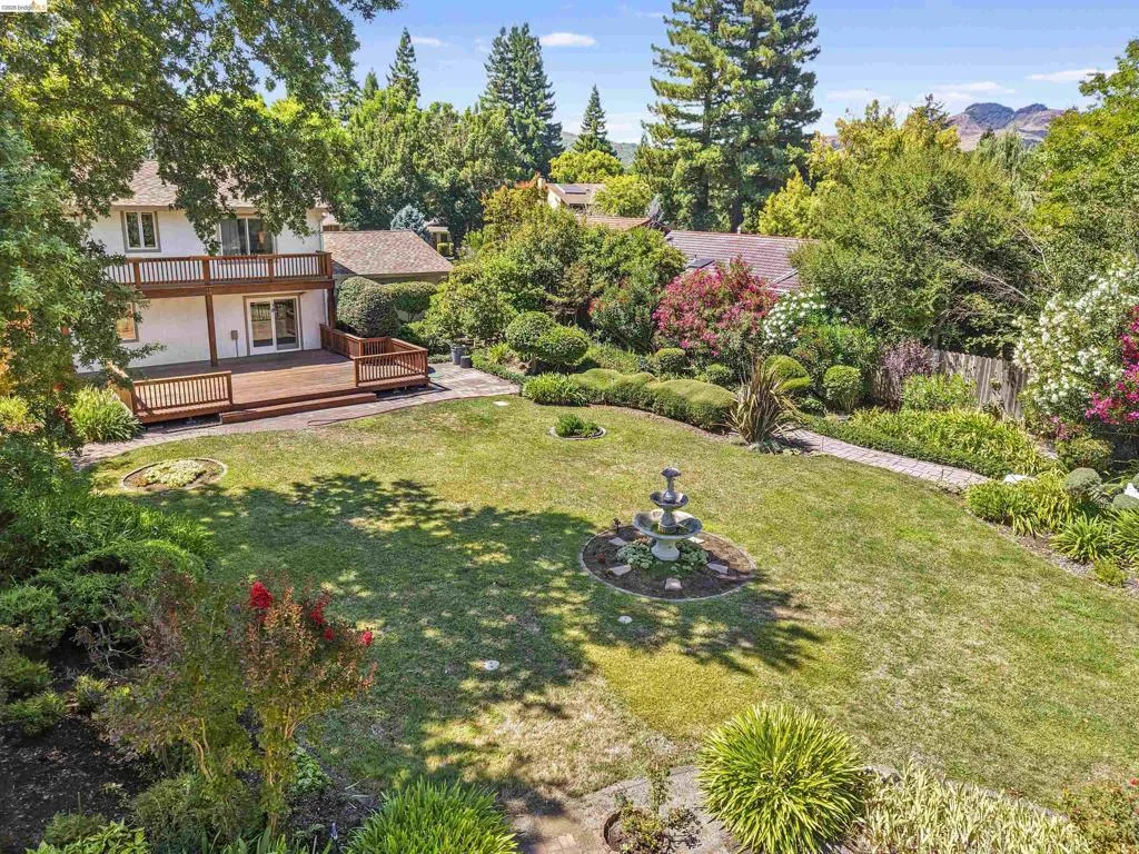 Expansive backyard featuring a multi-level wood deck, mature landscaping, a stone pathway, and a central tiered fountain