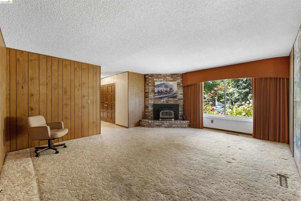 Spacious interior featuring a large picture window, a brick fireplace with a hearth, wood paneling, and textured ceilings