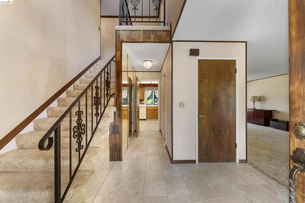 Entry foyer featuring tile flooring, a carpeted staircase with an ornate iron railing, and a wood-paneled accent wall