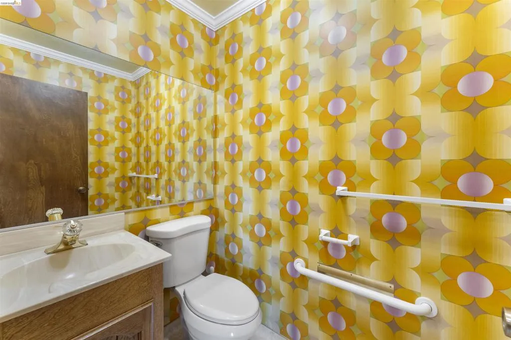 Bathroom featuring a vanity with an integrated sink, a large wall-mounted mirror, a two-piece toilet, and patterned wallpaper