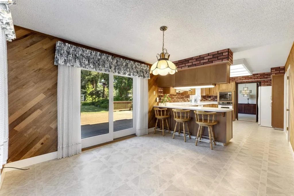 Kitchen and dining area featuring wood-finish wall paneling, a full-brick accent wall, and patterned flooring