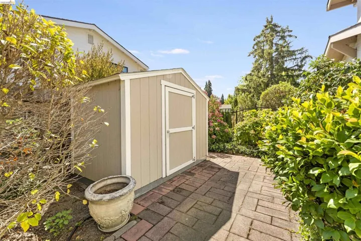 Gable-roofed storage shed with vertical siding and trim, positioned on a brick paver pathway