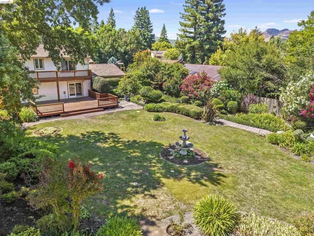 Expansive backyard featuring a multi-level wood deck, mature landscaping, a stone pathway, and a central tiered fountain
