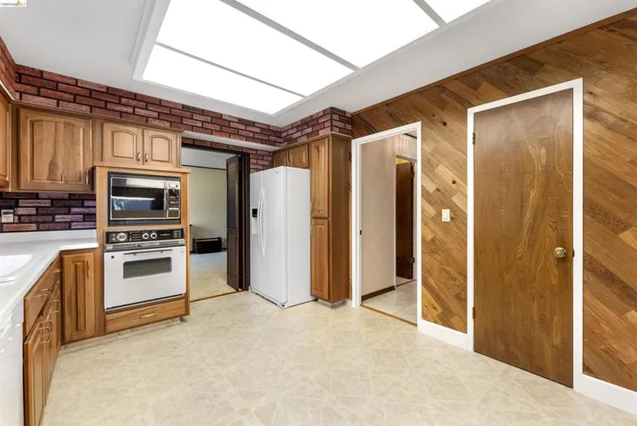 Kitchen featuring light wood cabinetry, white countertops, built-in microwave and oven, a white refrigerator, and recessed ceiling lighting