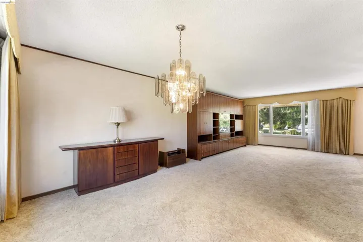 Spacious living area featuring a large picture window, light-colored carpeting, and a built-in wood-finish cabinet system