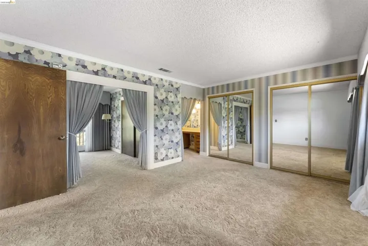 Expansive room with neutral carpeting and a textured ceiling