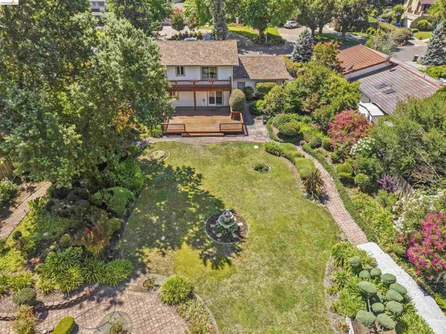 Expansive rear yard featuring a large wooden deck, manicured lawn, established garden beds, and mature trees