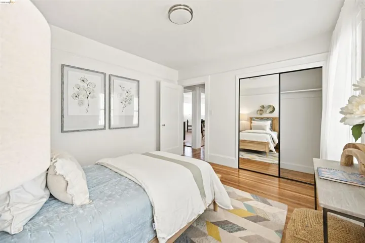 Bedroom featuring wood-finish flooring, a full-length mirrored closet door, a closet with built-in shelving, and white baseboards and trim
