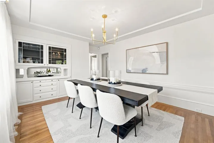 Dining room featuring a built-in buffet with glass-front cabinetry, detailed crown molding, a modern gold-toned chandelier, wood-finish flooring, and white wainscoting