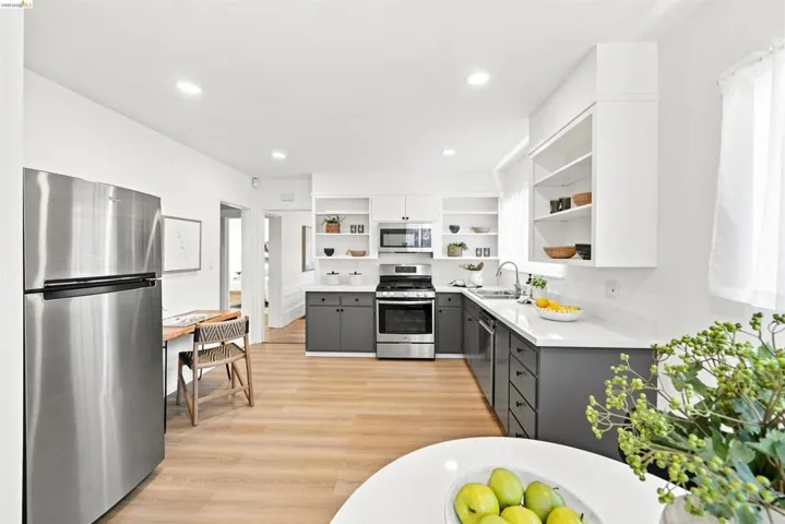 Modern kitchen featuring stainless steel appliances, two-tone cabinetry with open shelving, light-finish flooring, and recessed lighting