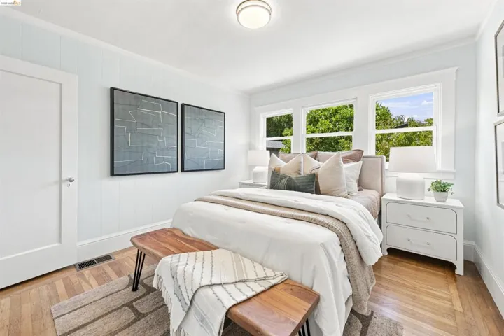 Bedroom featuring three windows, wood-finish flooring, and white paneled walls