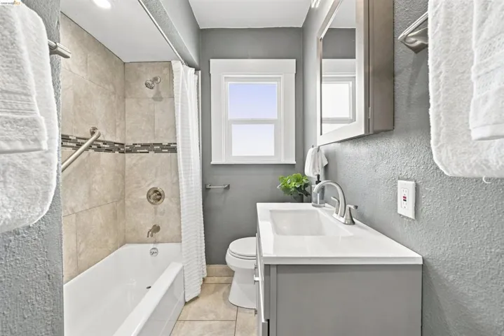 Bathroom featuring a white bathtub with tiled shower surround, a single sink vanity with a white countertop, and a window providing natural light