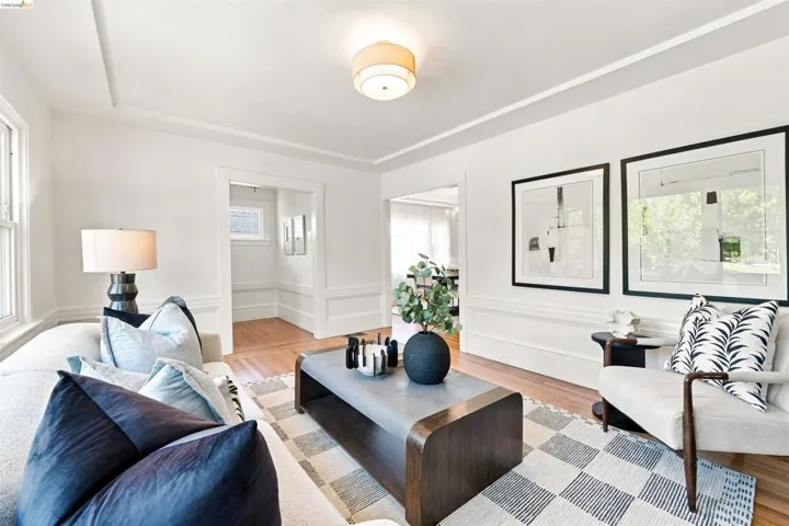 Living area featuring light wood-finish flooring, white walls, and a tray ceiling with a flush-mount light fixture