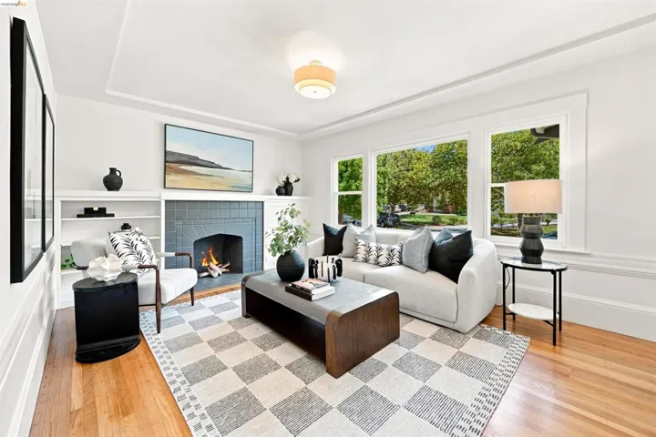 Living room featuring hardwood flooring, a fireplace with dark tile surround, built-in shelving, extensive window-framing, and crown molding