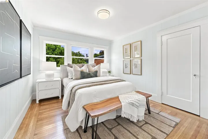 Light-filled bedroom featuring wood-finish flooring, multiple windows, vertical paneling, and a flush mount ceiling fixture