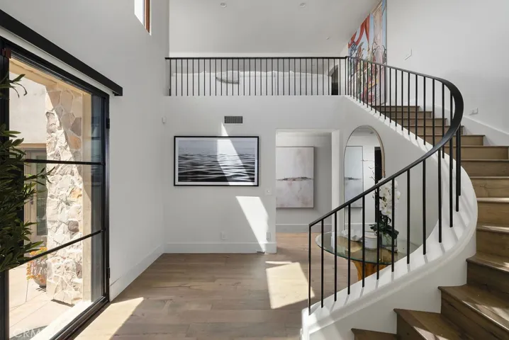 Light-filled entry foyer featuring a dramatic curved staircase, custom iron railing, wide-plank wood flooring, and direct access to the private courtyard.