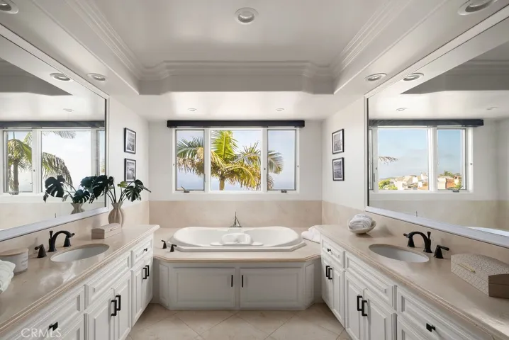 Spacious ocean-view primary bathroom featuring dual vanities and a separate soaking tub framed by picturesque coastal views.