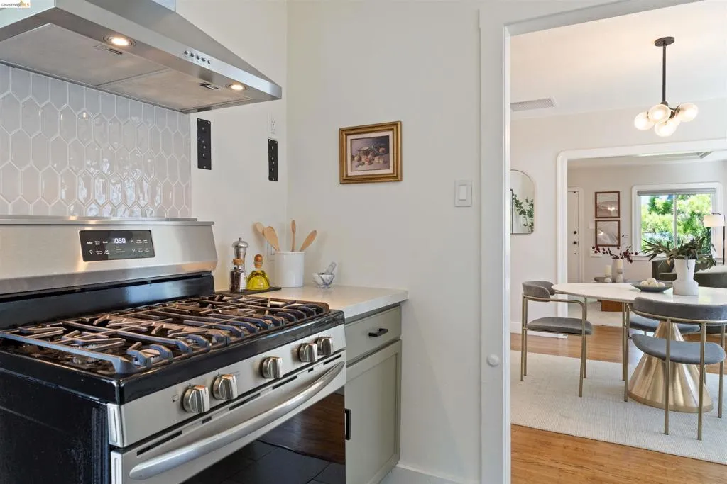 Stainless steel gas range with coordinating ventilation hood, complete with a geometric white tile backsplash and light-toned countertop