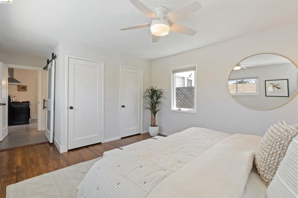 Primary bedroom has hardwood floor, a ceiling fan, multiple windows, two closets, and an ensuite bathroom.