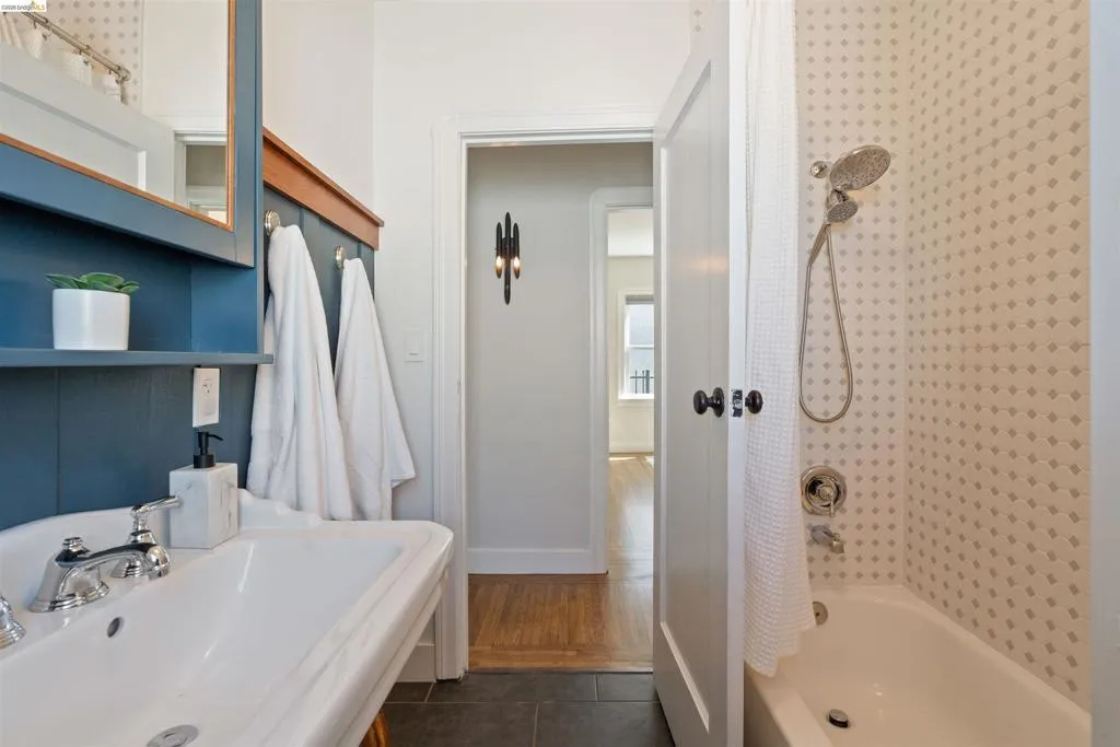 Hall Bathroom featuring a white porcelain sink with chrome fixtures, a blue paneled vanity with integrated shelving, and a tiled shower/tub combination with a handheld showerhead