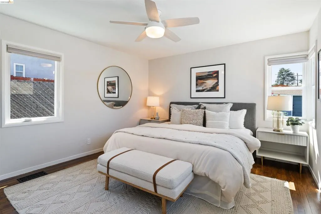 Primary bedroom has hardwood floor, a ceiling fan, multiple windows, two closets, and an ensuite bathroom.