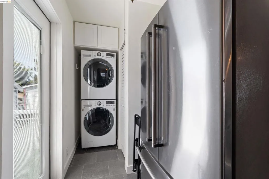 Laundry area featuring stacked front-load washer and dryer, upper cabinetry is in the back of the kitchen extension.