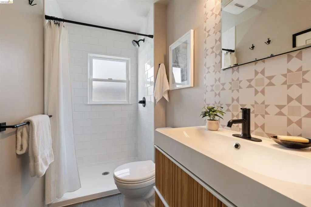 Ensuite Bathroom featuring a patterned tile wall, a contemporary vanity with an integrated sink, matte black fixtures, a built-in shower with white subway tile, and a privacy window