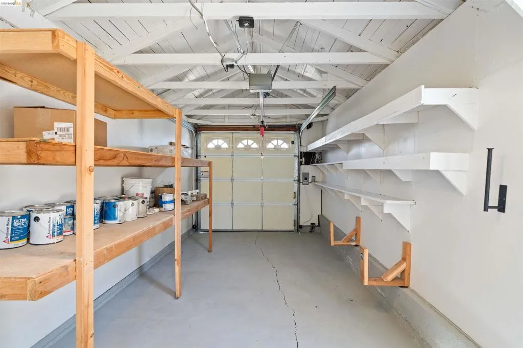 Garage interior featuring exposed white-painted ceiling rafters, a concrete floor, and a white paneled garage door with arched window details