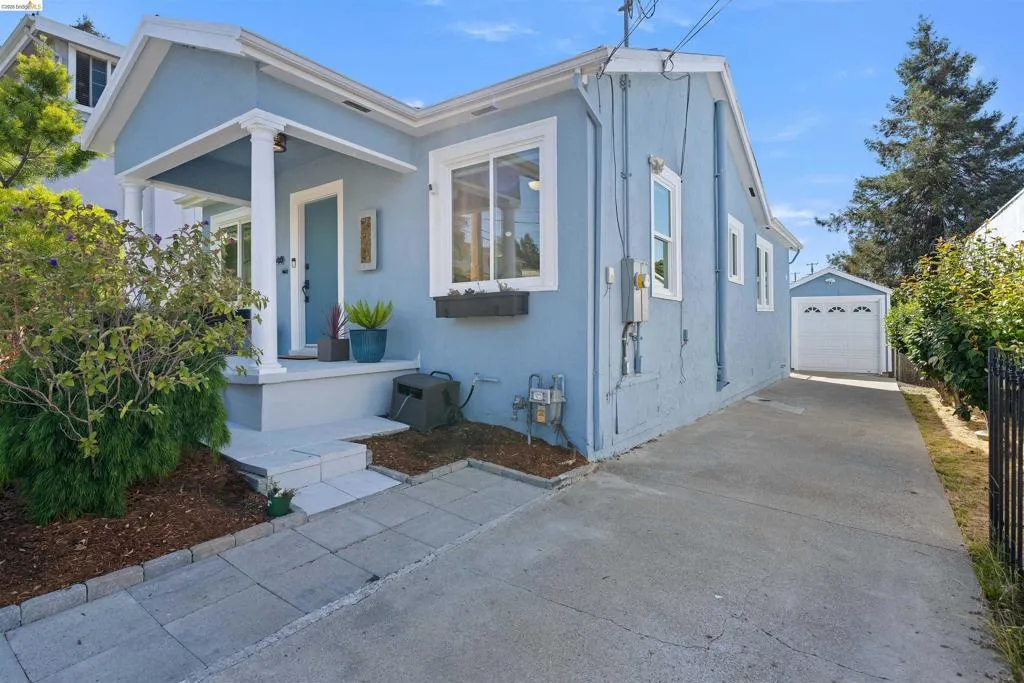 Charming light blue exterior featuring a covered front porch with white columns, a long concrete driveway, and a detached garage
