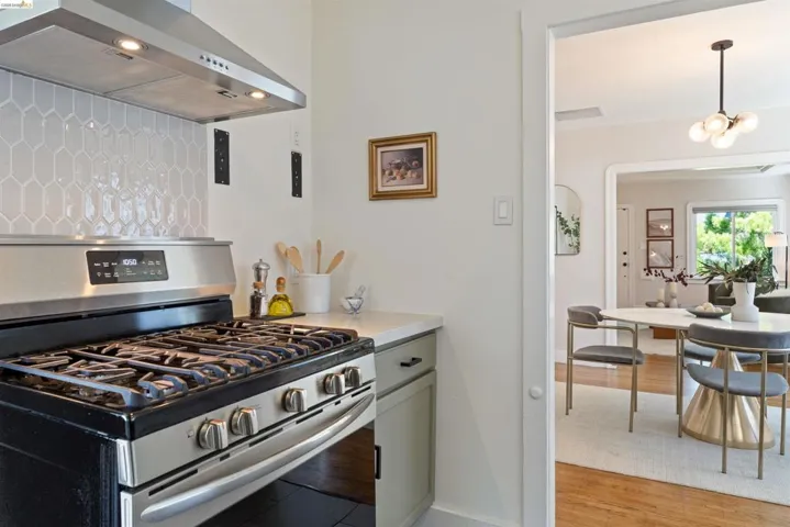 Stainless steel gas range with coordinating ventilation hood, complete with a geometric white tile backsplash and light-toned countertop