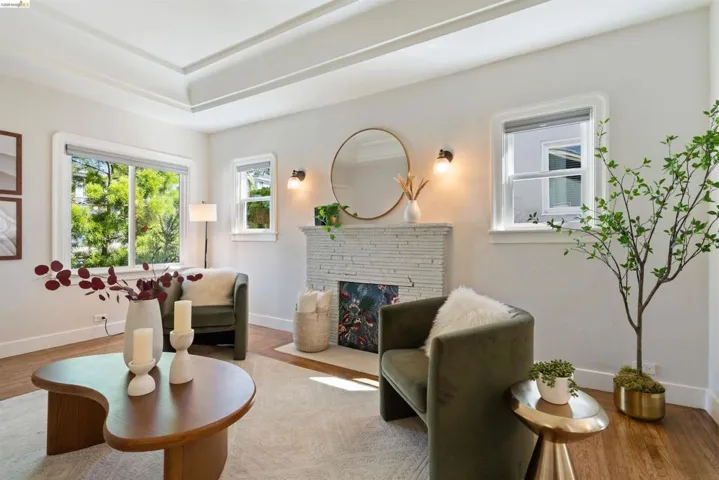 Living area featuring a tray ceiling, recessed fireplace with stacked stone surround, wood-finish flooring, white baseboards, and multiple​​‌​​​​‌​​‌‌​​‌​​​‌‌​​​‌​​‌‌​​‌‌​​‌‌​​​​ windows