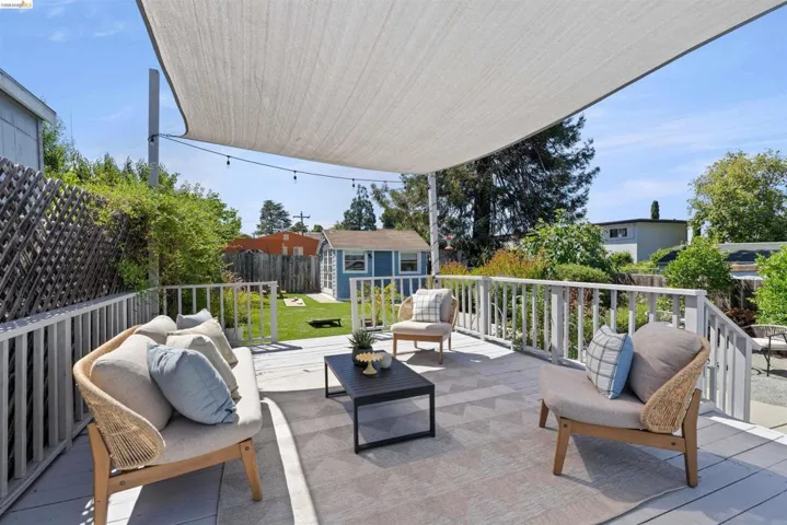 Expansive outdoor deck featuring a shade sail, string lighting, painted wooden railings, and steps descending to a private, fenced backyard with a garden office