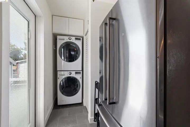 Laundry area featuring stacked front-load washer and dryer, upper cabinetry is in the back of the kitchen extension.