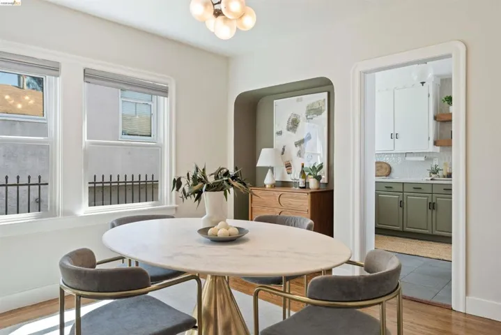 Dining room features harwood floor, dual-pane windows with roller shades, an arched wall niche, and an adjoining kitchen with white upper and green lower cabinetry