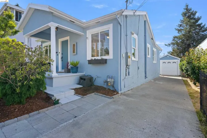 Charming light blue exterior featuring a covered front porch with white columns, a long concrete driveway, and a detached garage