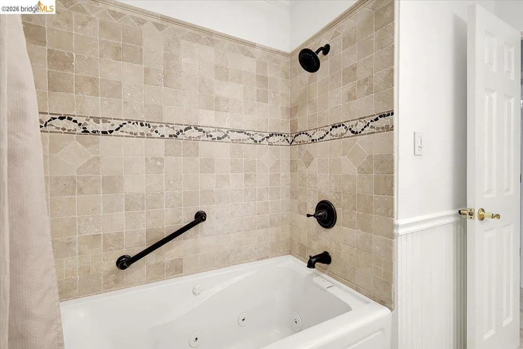 Jetted bathtub with full-height tile surround featuring a decorative mosaic accent band