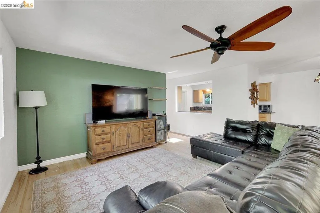 Living area featuring wood-finish flooring, a ceiling fan with wood-look blades, and a pass-through window to the kitchen