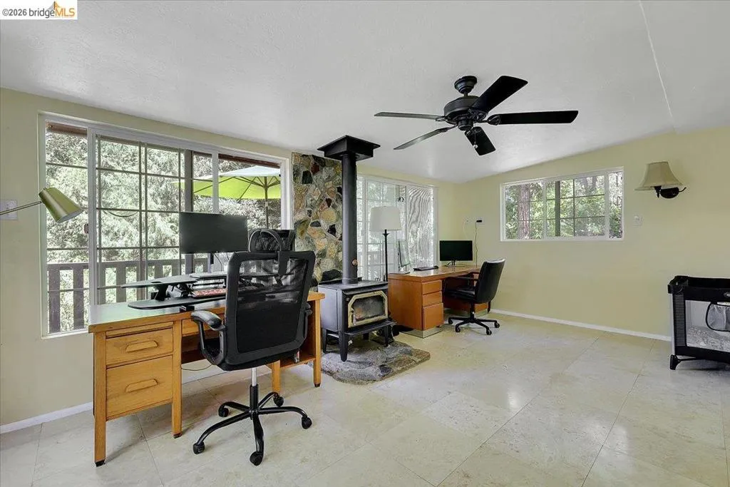 Spacious room featuring multiple windows, a stone-faced fireplace with a wood-burning stove, and tiled flooring