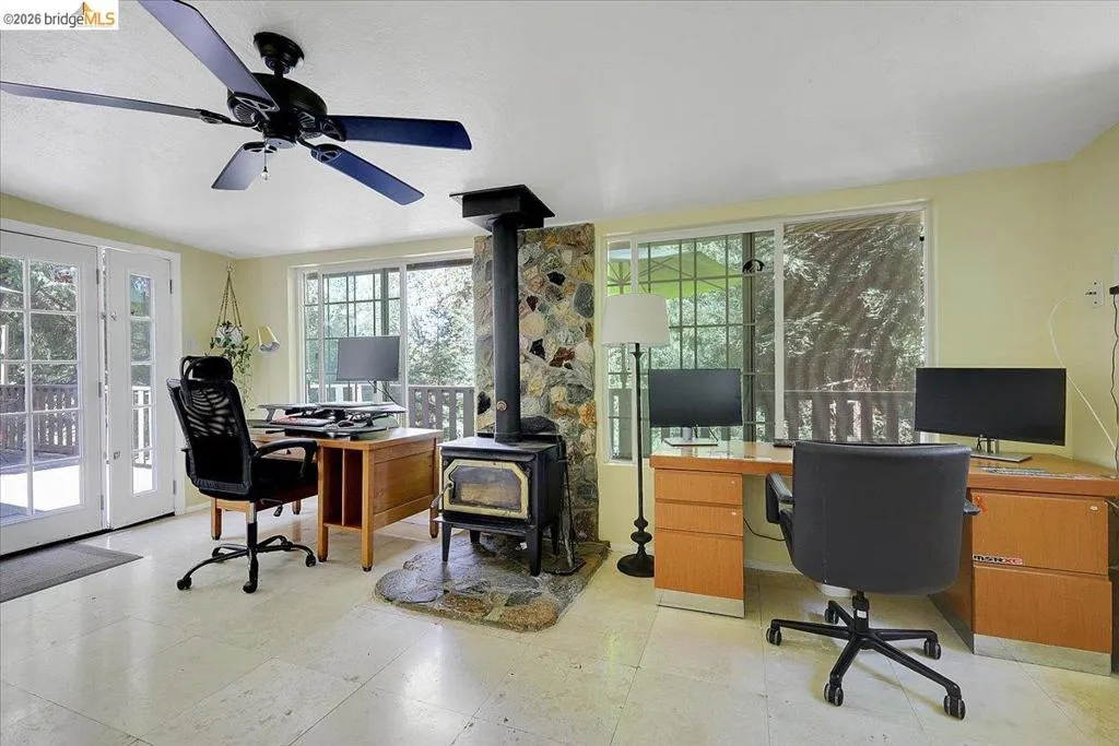 Room featuring a stone-clad wood-burning stove with a stone hearth, white tile flooring, and multiple windows